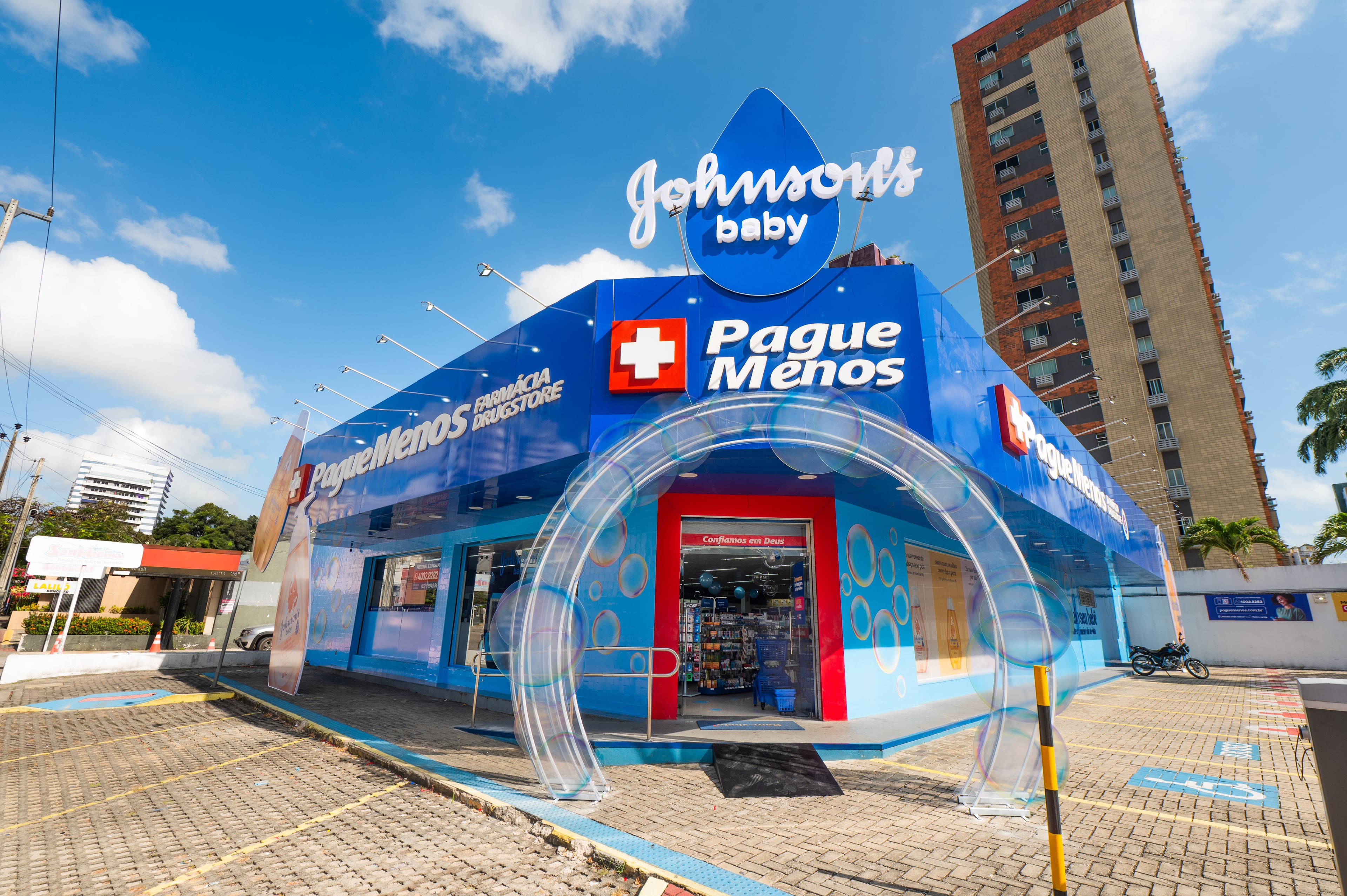 Fachada azul de unidade Pague Menos com letreiros e portal transparente na entrada
